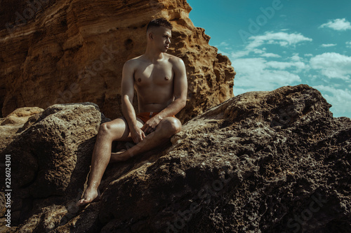 Canvas Print Strong face muscle male model on the nature background with sand stones and wate