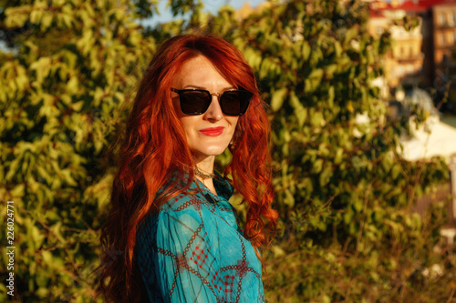 Portrait of a beautiful girl with red hair in a birch blouse on the background of the city