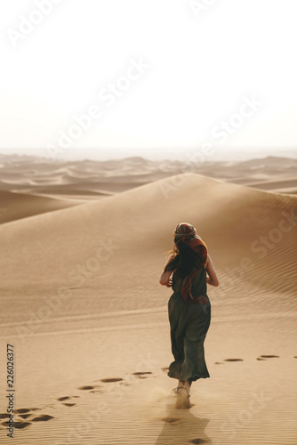 women is running towards the landscape of dune desert, with footprints