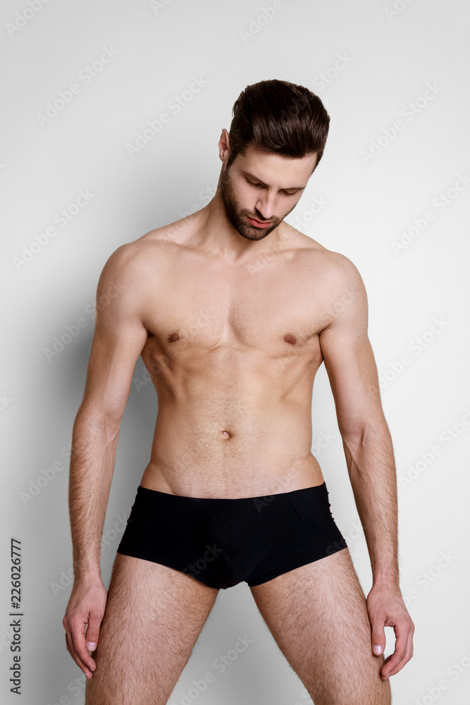 Handsome muscled strong face stripped male model in black underwear on white isolated font background