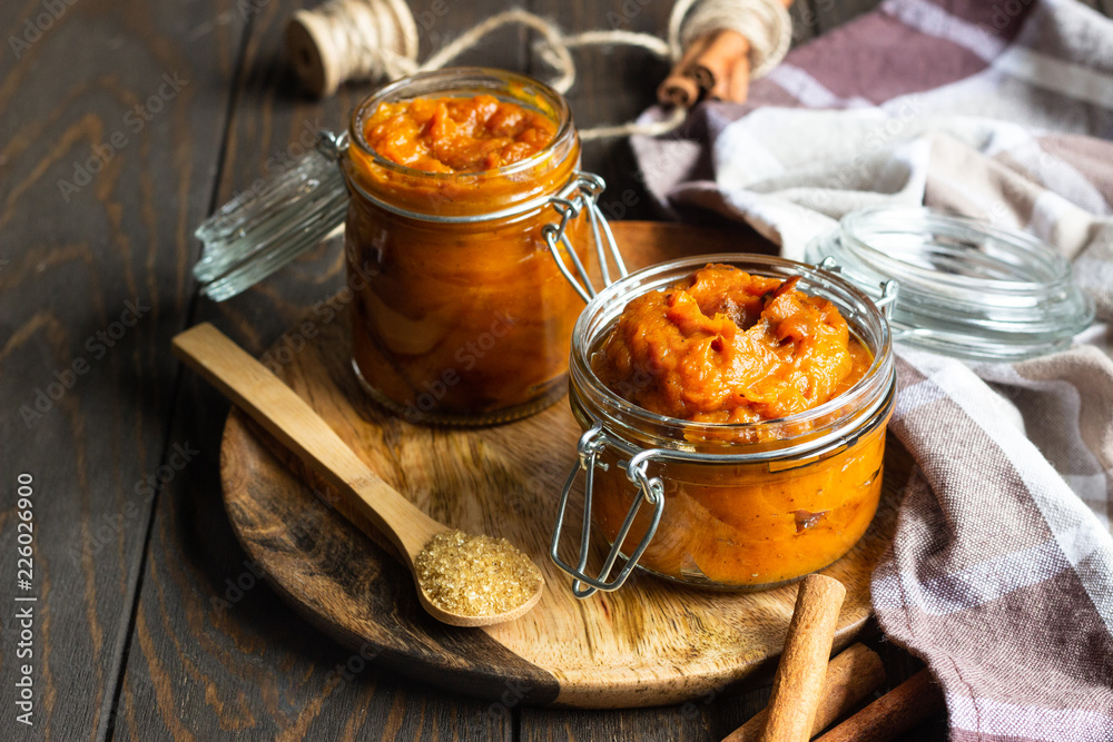 Pumpkin butter in glass jar with cinnamon sticks and sugar on old wood background, selective focus. Pumpkin butter in glass jar with cinnamon sticks and sugar on old wood background, selective focus.