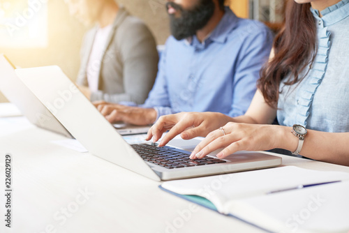 Close-up of business people sitting in a row and typing on laptop while sitting at office desk