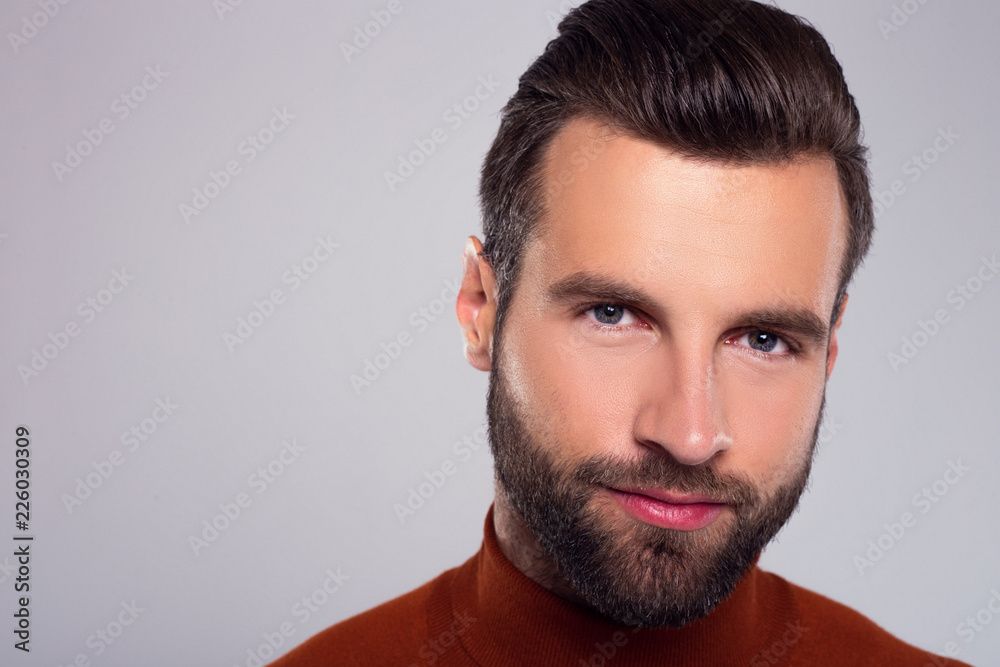 Portrait of real masculinity. Close-up of handsome young man looking at camera with smile while standing against white background Portrait of real masculinity. Close-up of handsome young man looking at camera with smile while standing against white background
