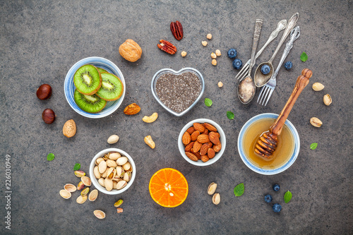 Ingredients for a healthy foods background, nuts, honey, berries, fruits, blueberry, orange, almonds, walnuts and chia seeds .The concept of healthy food set up on dark stone background. Flat lay .