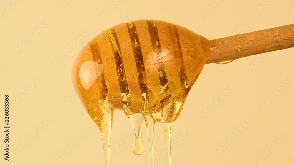 Close up honey flowing from wooden dipper on beige