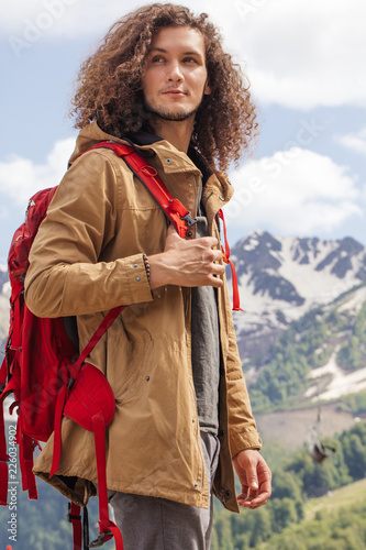 Young long curly haired man standing on summer mountains background and enjoying