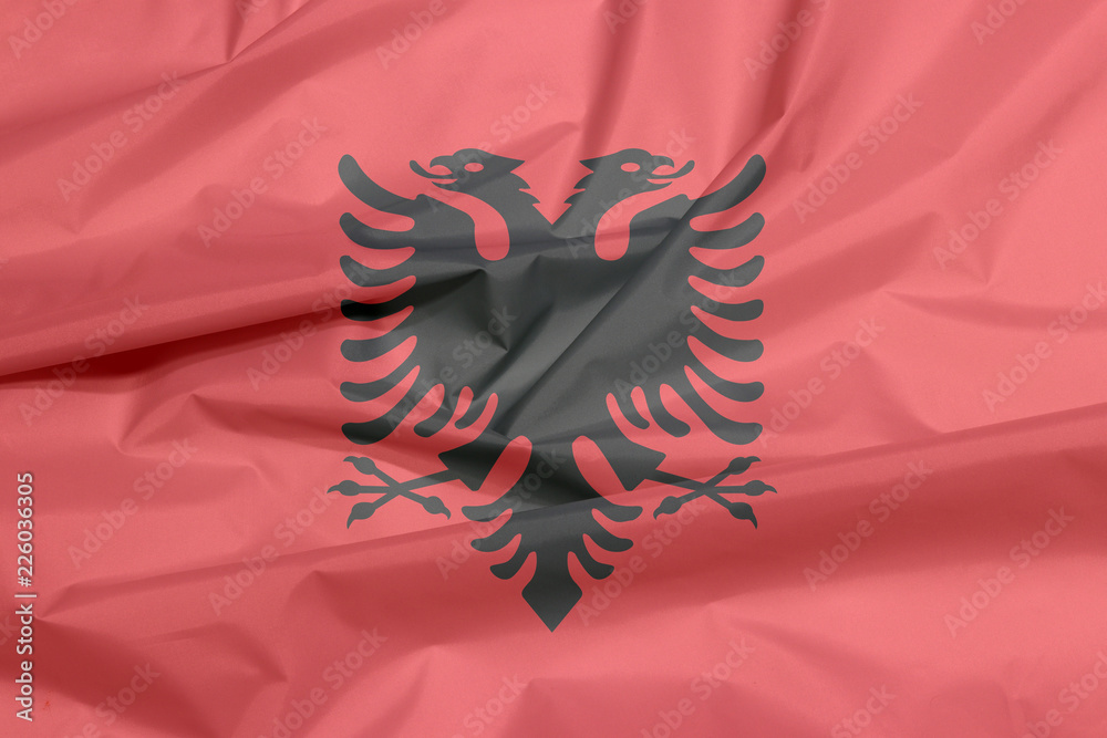Fabric flag of Albania. Crease of Albanian flag background, a red field with the black double-headed eagle in the center. Fabric flag of Albania. Crease of Albanian flag background, a red field with the black double-headed eagle in the center.