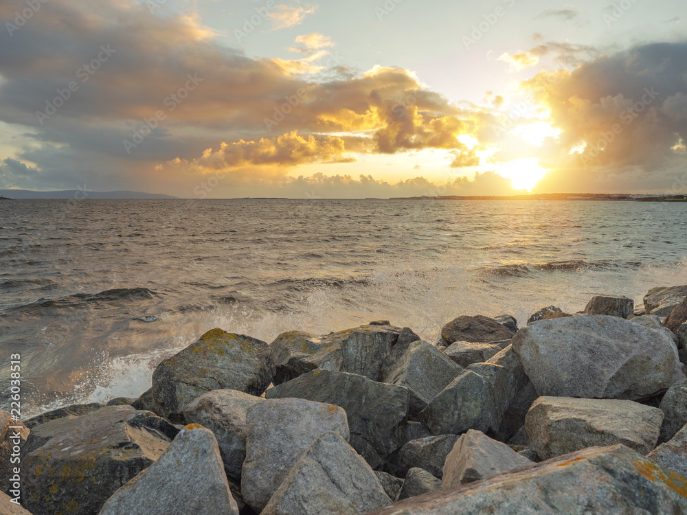 Sunset over the ocean, wave hits rocks creating splash of water. Sunset over the ocean, wave hits rocks creating splash of water.