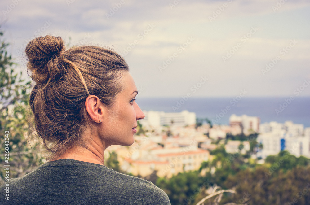 A woman stares into the distance to the sea horizon and the city in front of him