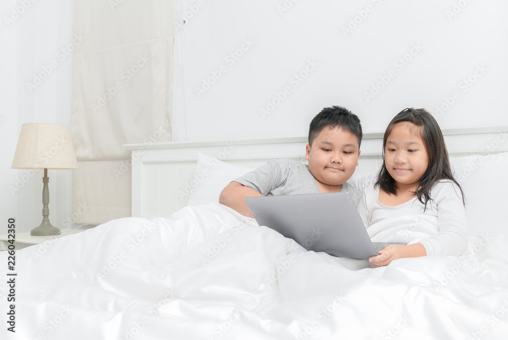 Brother and sister play laptop on bed together Brother and sister play laptop on bed together