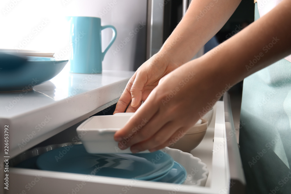 Woman putting ceramic dish into kitchen drawer