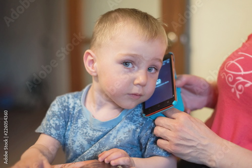 Obraz na plátně A little boy, 1,5 years old, sits on the woman's lap and listens to a mobile phone