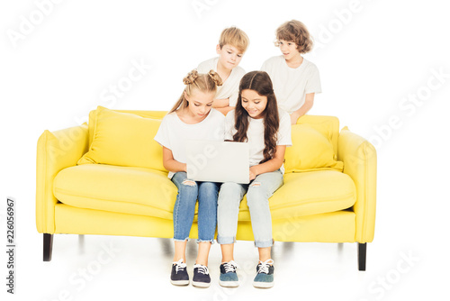 smiling friends using laptop on yellow sofa isolated on white