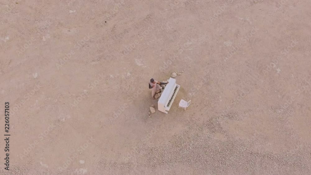 Surreal story- girl near the white piano in the desert against the background of mountains and stones. Unusual plot. Aerial view. View from above Surreal story- girl near the white piano in the desert against the background of mountains and stones. Unusual plot. Aerial view. View from above
