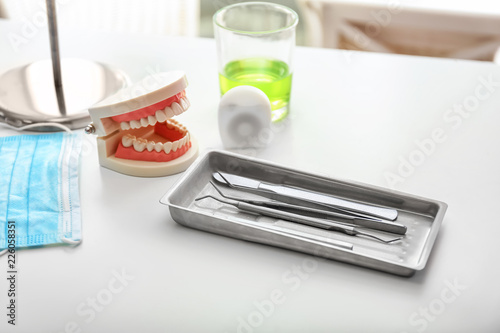 Tray with dentist's tools, mask and artificial jaw on light table in doctor's office