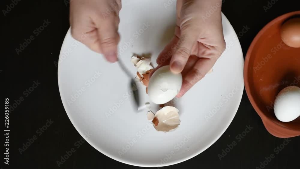 Hands off the egg-shell of chicken eggs at home Remove the eggshell from the eggs of different colors of white and brown on a white plate on a black table 