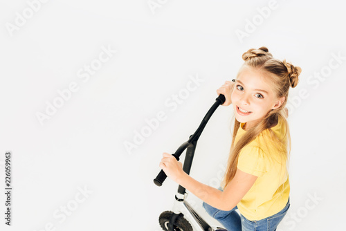 high angle view of adorable happy kid riding scooter and smiling at camera isolated on white