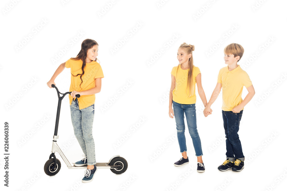 happy child riding scooter and looking at friends holding hands isolated on white happy child riding scooter and looking at friends holding hands isolated on white