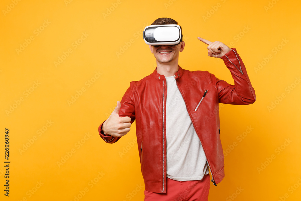 Portrait vogue handsome young man in red leather jacket, t-shirt looking in headset standing isolated on bright trending yellow background. People sincere emotions lifestyle concept. Advertising area.