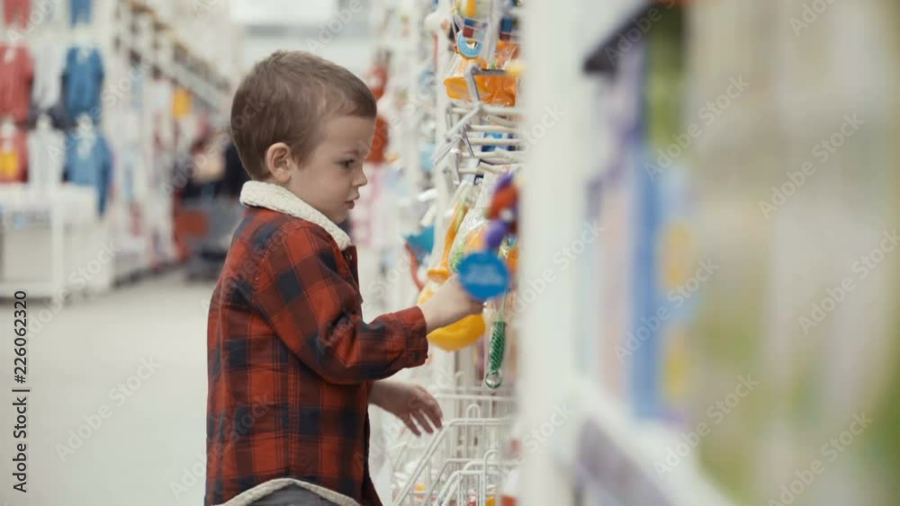 Little boy is standing of the shop and choosing toys Little boy is standing of the shop and choosing toys