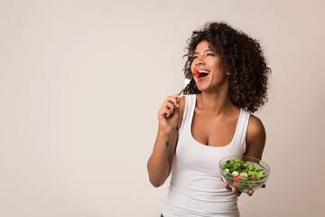 Excited lady eating healthy salad over light background