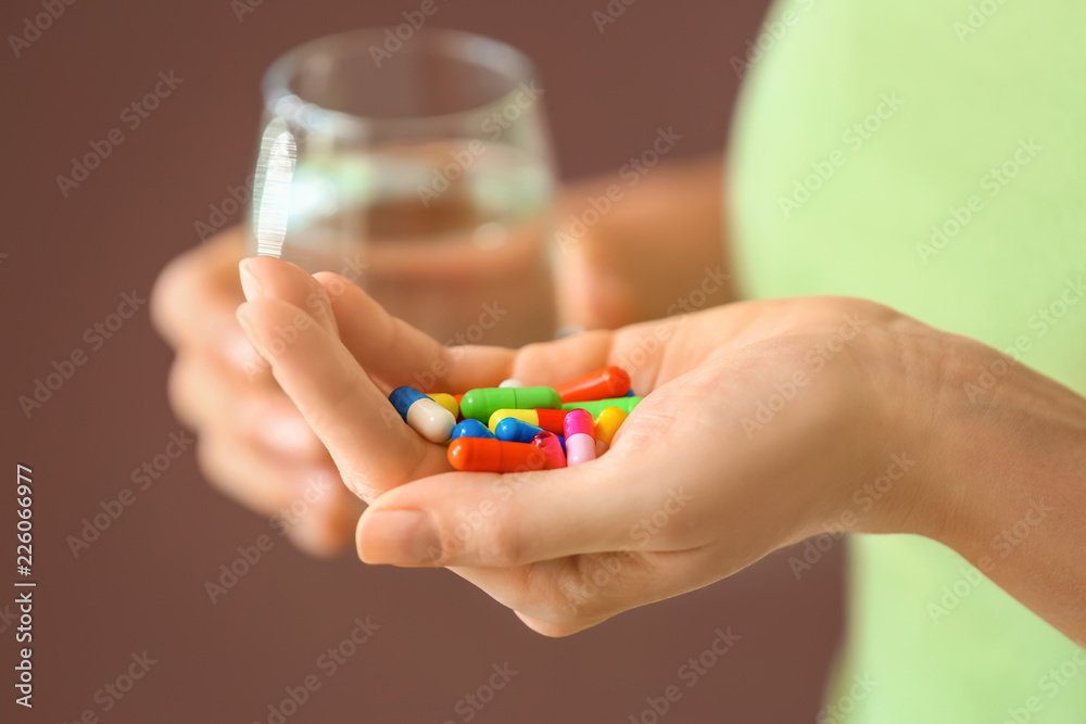 Woman holding pills and glass of water on color background, closeup Woman holding pills and glass of water on color background, closeup