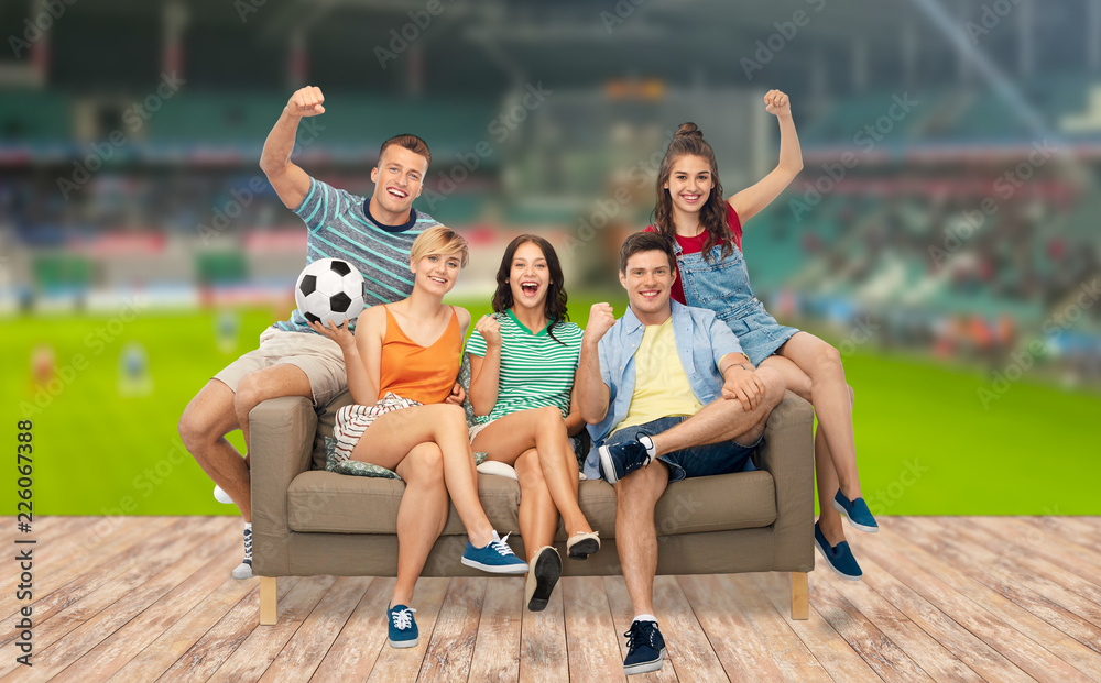 entertainment, leisure and people concept - group of happy smiling friends or fans with soccer ball sitting on sofa over football field background
