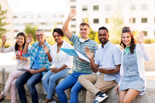 education, international and people concept - group of happy exchange students with notebook and takeaway drinks waving hands outdoors photo