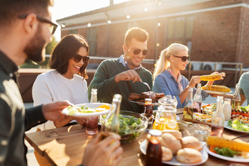 leisure and people concept - happy friends eating and drinking at barbecue party on rooftop in summer