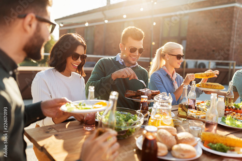 leisure and people concept - happy friends eating and drinking at barbecue party on rooftop in summer