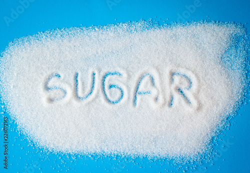The word sugar write on a pile of white sugar with blue background