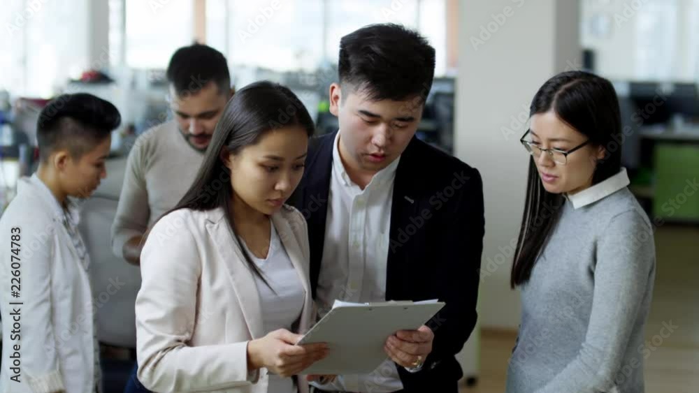 Three business people standing next to each other and discussing work using documents attached to clipboard, medium shot Three business people standing next to each other and discussing work using documents attached to clipboard, medium shot