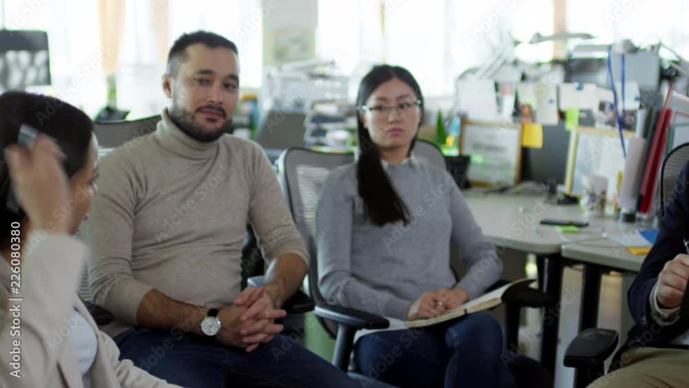 Tracking shot of group of young Asian employees sitting in chairs and discussing project when working in office Tracking shot of group of young Asian employees sitting in chairs and discussing project when working in office