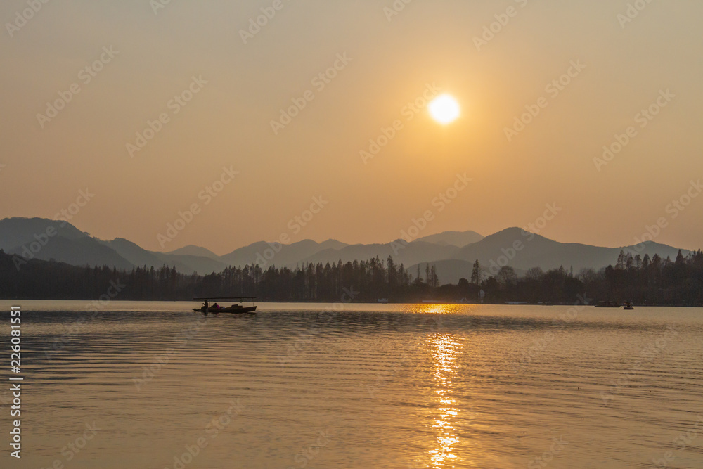 Boat traveling on West Lake under sunset in Hangzhou