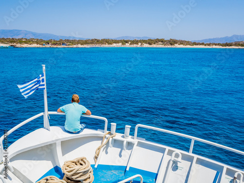 Greek flag waving on the bow of a boat sailing toward the island of Chrissi. The uninhabited island of Chrissi is available only by boat, an hour of cruise from Ierapetra, south of Crete.