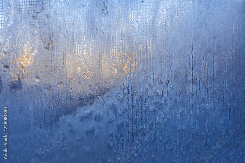 Blue frozen glass with striped frosty pattern and winter sun outside. © SeNata