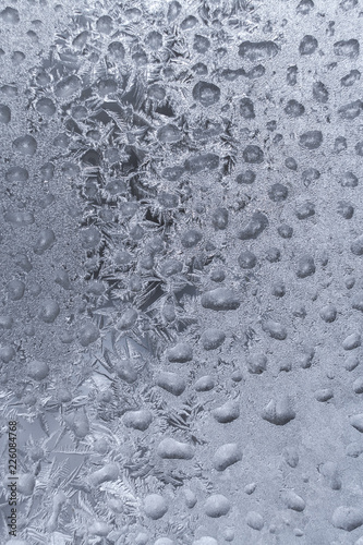 White frosty pattern formed from lot of frozen water drops on winter window.
