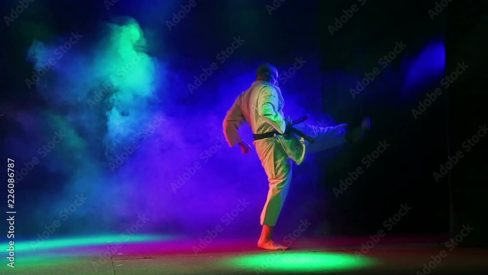 A man is engaged in karate on a black background with colored smoke
