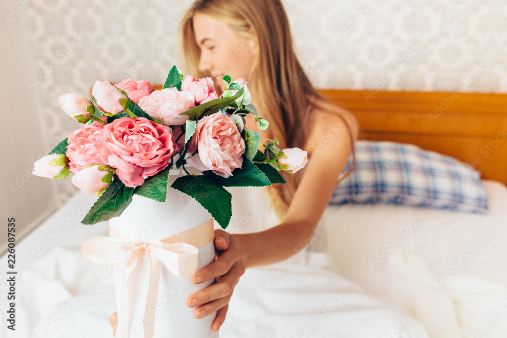 beautiful girl with peony flowers sitting on the bed. She just woke up and got a bouquet of flowers