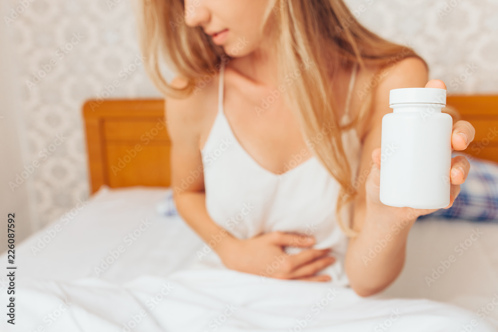Young girl hands holding her belly, and holds pills in her hand from the pain of sitting in bed and not feeling well, Young girl hands holding her belly, and holds pills in her hand from the pain of sitting in bed and not feeling well,
