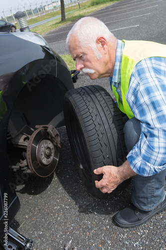 aged man changing leaking tire on the verge © auremar