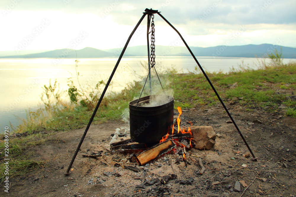 Cooking in a pot on a fire on the shore of the lake. Close-up. Landscape. Background. Cooking in a pot on a fire on the shore of the lake. Close-up. Landscape. Background.