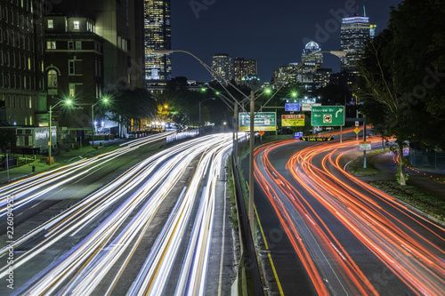 Boston, Massachusetts skyline at night, featuring car lights trails on the foreground and illuminated buildings on the background