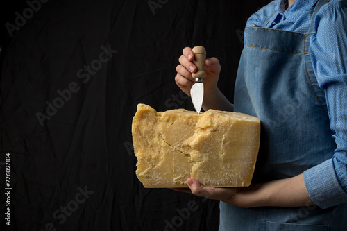 Woman holding knife and a slice of parmesan cheese on black background