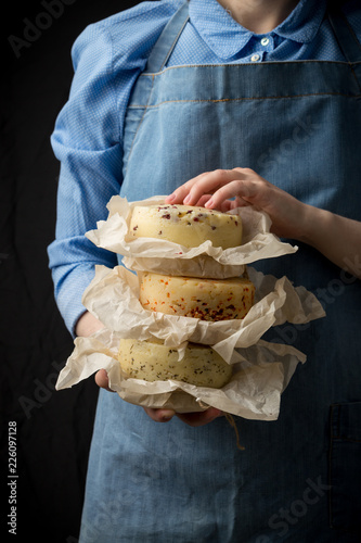 Woman holding assorted cheese head in blue apron on dark background