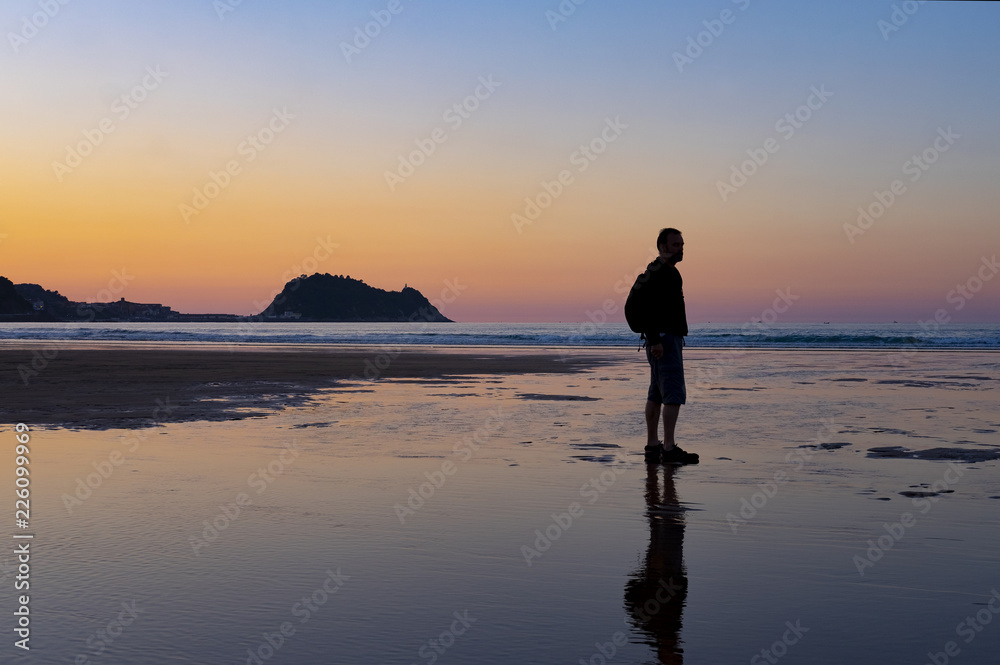 Man on the beach of Zarautz at sunset with the island of Getaria in the background.