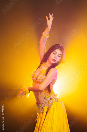 Fotografie Alluring sexy traditional oriental belly dancer girl dancing on yellow neon smoke background