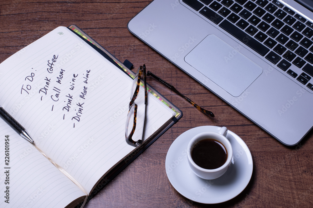 Woodgrain Table with Computer, espresso coffee in a white cup on a white saucer, Glasses, Pen and Notebook. Woodgrain Table with Computer, espresso coffee in a white cup on a white saucer, Glasses, Pen and Notebook.