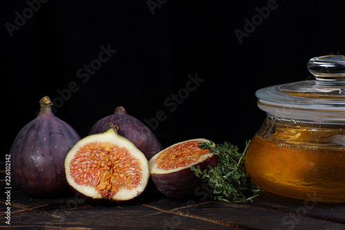 Purple figs whole and cut on a dark background next to a jar of linden honey photo