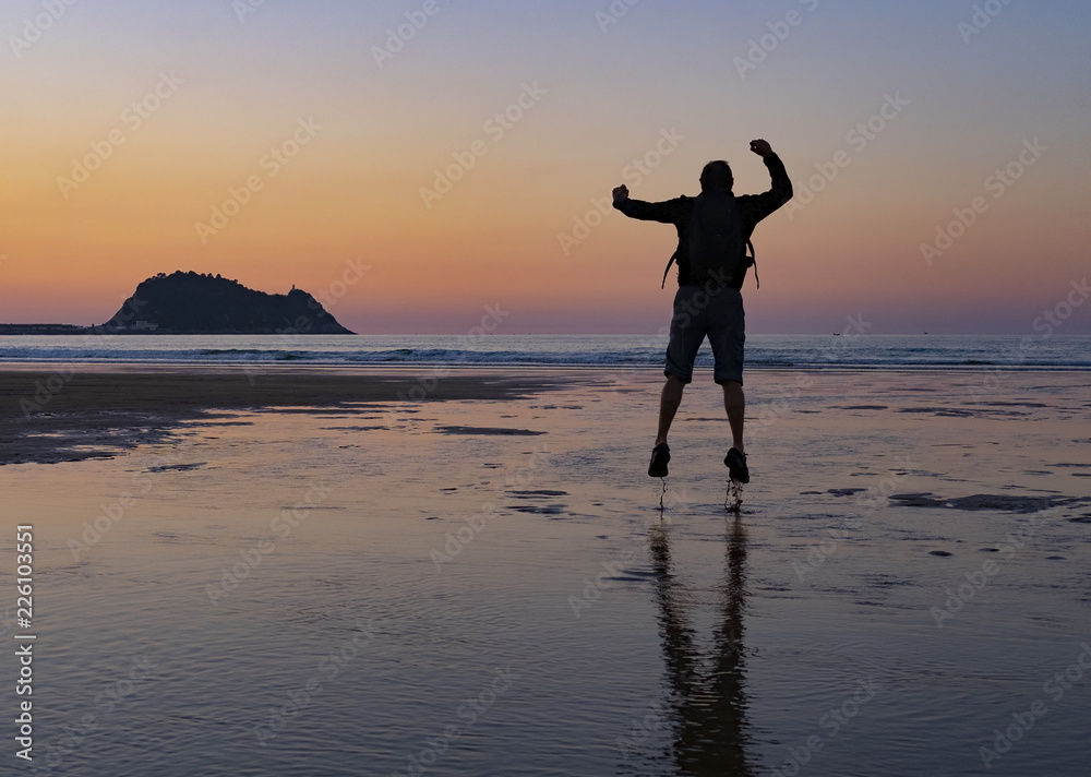 Man on the beach of Zarautz at sunset with the island of Getaria in the background.